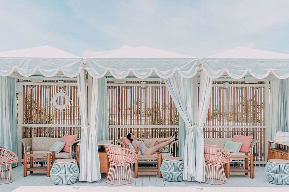 Beachfront cabana lounge with white curtains, mint green railings, and ocean views