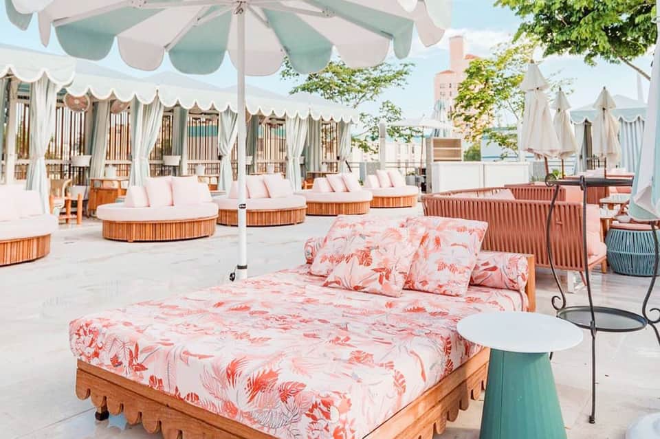Elegant outdoor lounge area with white umbrellas, coral bedding, and draped seating structures