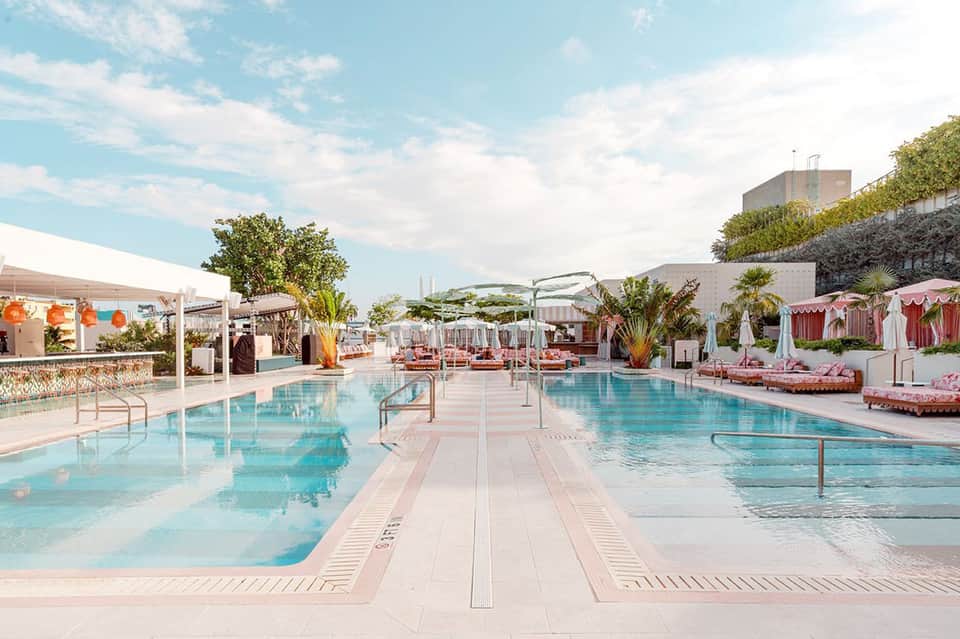 Luxury resort outdoor pool deck with lounge chairs, umbrellas, and pink cabanas under blue sky
