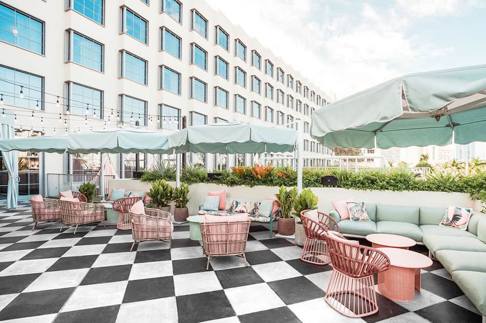 Rooftop terrace with pink and white wicker chairs, green umbrellas, and modern building