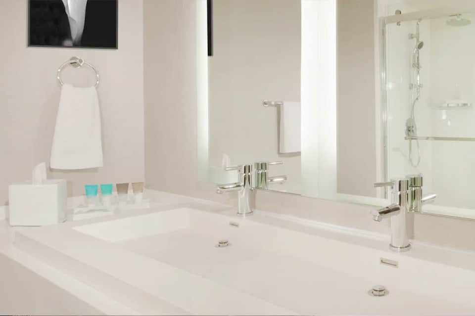Modern bathroom with dual vanities, white countertops, and walk-in shower