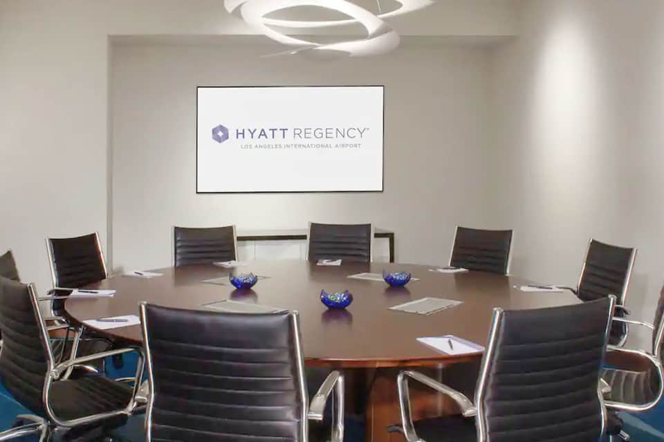 Conference room with oval table, black chairs, and Hyatt Regency LAX sign on wall