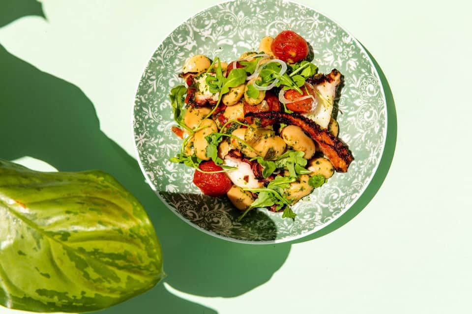 Grilled seafood and mushroom dish on decorative green plate with fresh greens