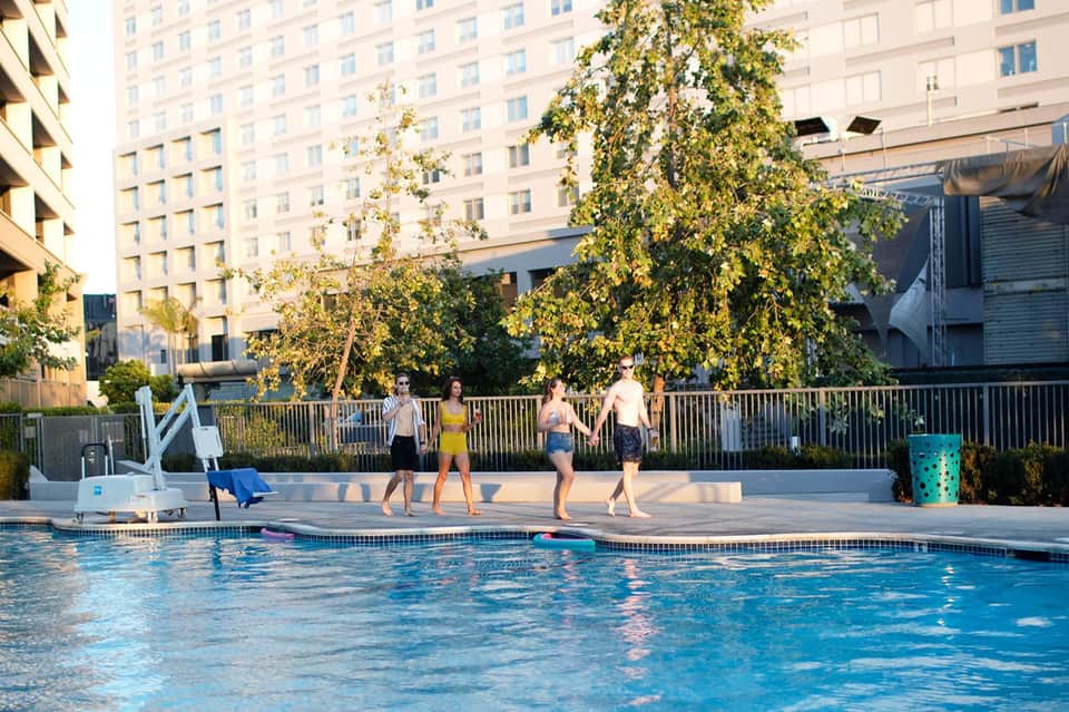 Group of people walking poolside with city buildings and trees in background