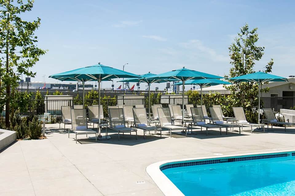 Resort pool deck with turquoise umbrellas, lounge chairs, and city skyline view