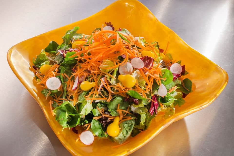 Colorful salad with shredded carrots, mixed greens, and corn on yellow plate