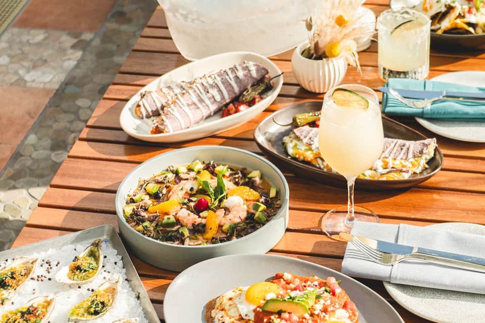 Beachside dining table with grilled seafood, fresh salads, and cocktails on a wooden deck
