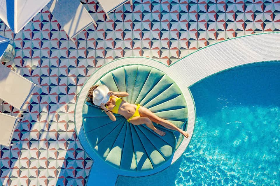 Woman in yellow bikini floating on circular pool float in geometric-tiled resort pool