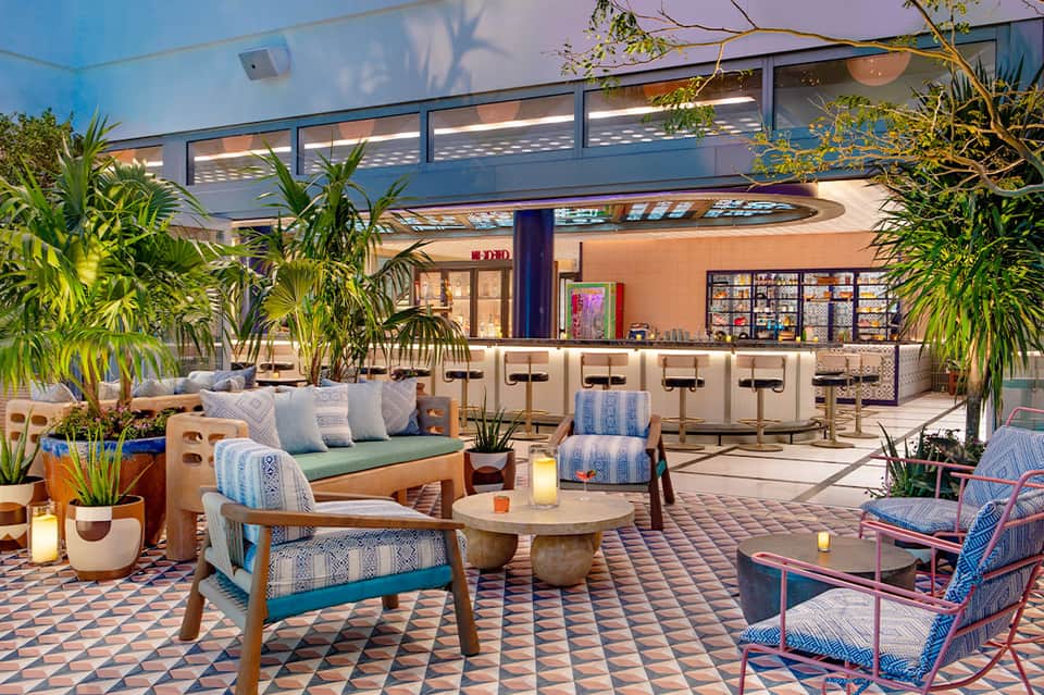Modern resort lounge with blue-upholstered seating, potted plants, and geometric floor tiles