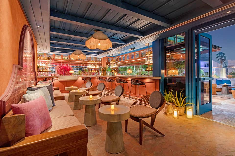 Modern lounge bar with orange accents, ambient lighting, and views of palm trees at dusk