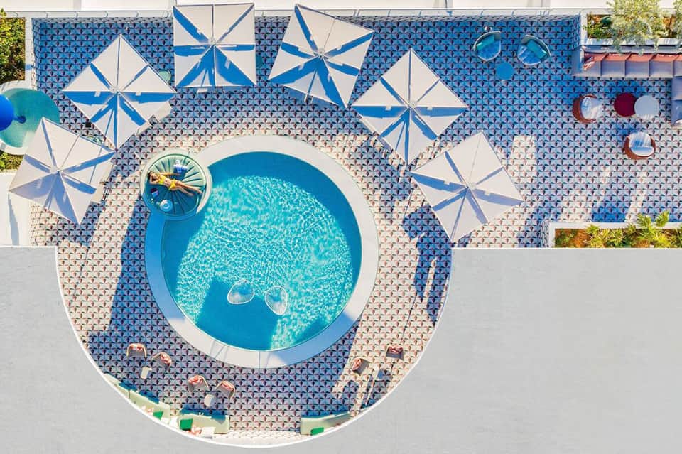 Aerial view of circular swimming pool surrounded by striped umbrellas and patterned deck