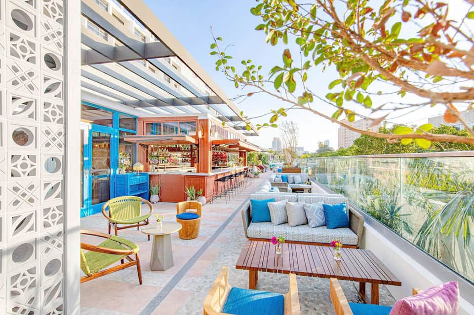 Colorful rooftop bar and lounge area with blue and orange accents, seating, and city skyline views.