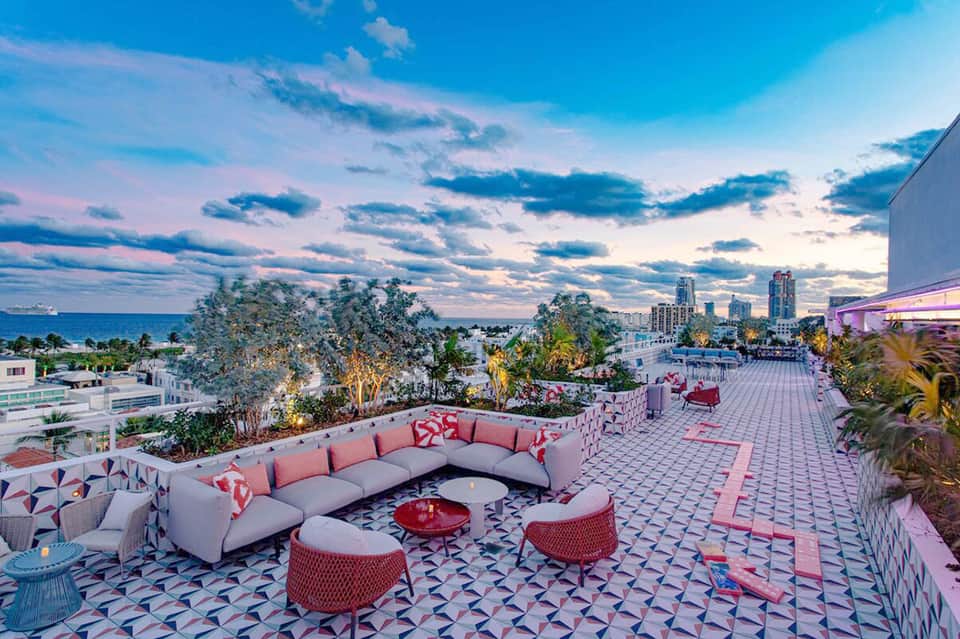 Rooftop lounge with curved seating, fire pit, and cityscape view at sunset