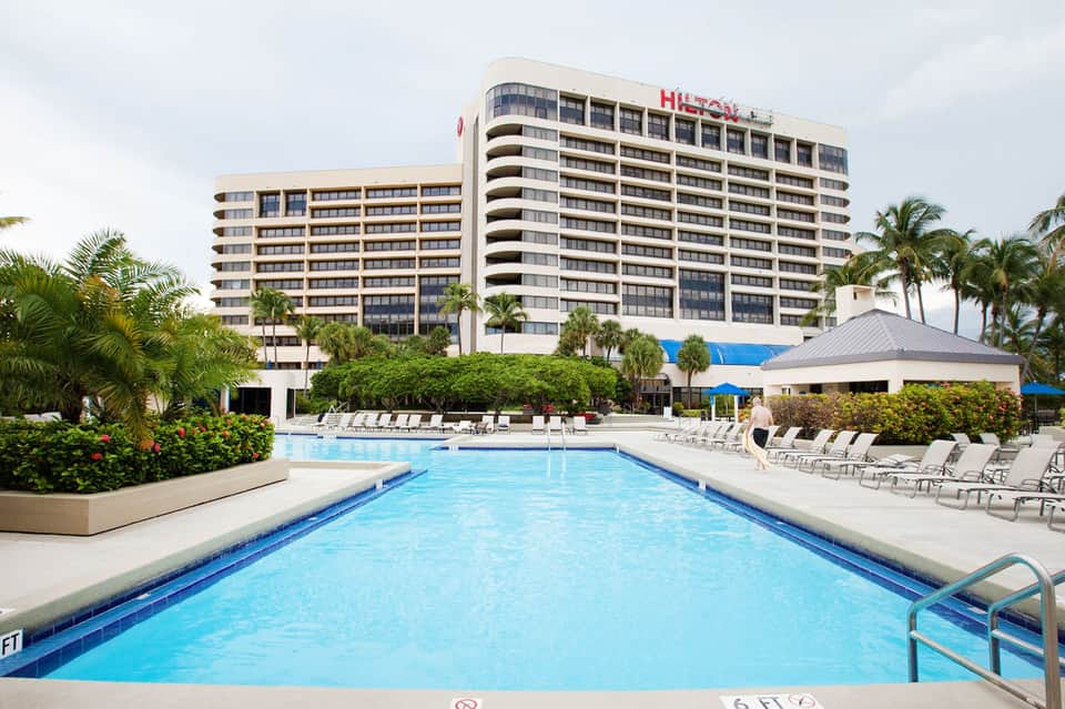 Beachfront hotel with multiple pools, palm trees, and waterfront landscaping