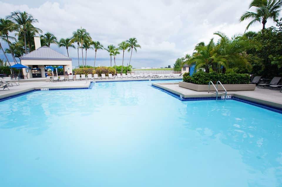 Resort swimming pool with clear blue water, palm trees, poolside cabanas, and tropical landscaping