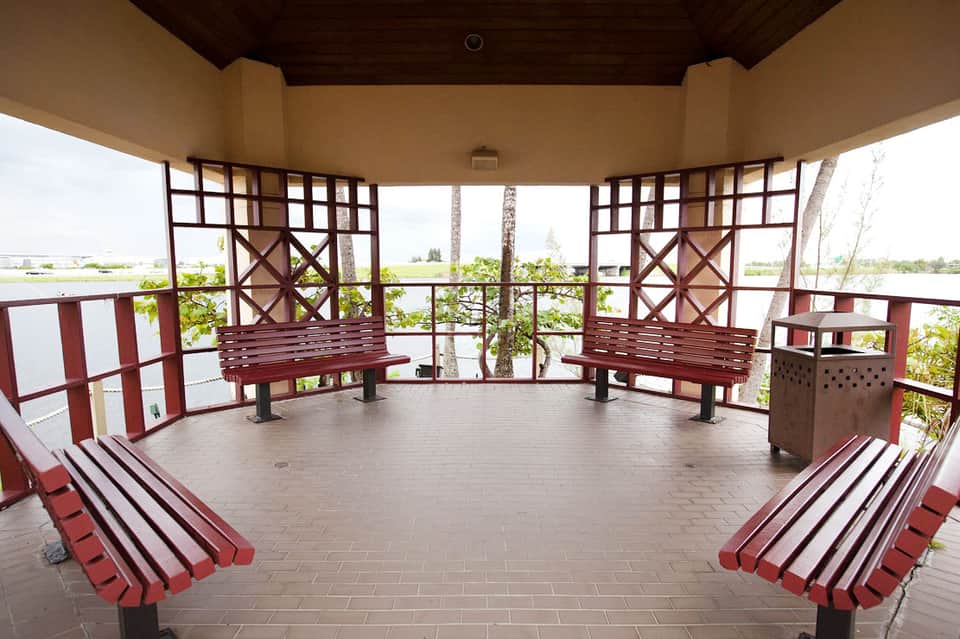 Covered pavilion with red wooden benches overlooking a flat landscape with palm trees