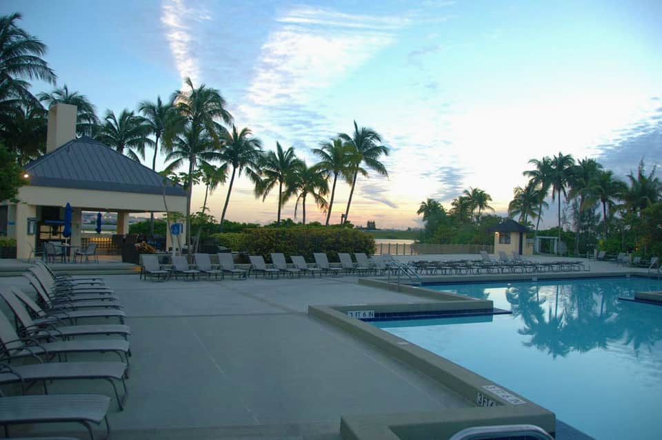 Evening poolside view with palm trees, lounge chairs, and waterfront gazebo at dusk