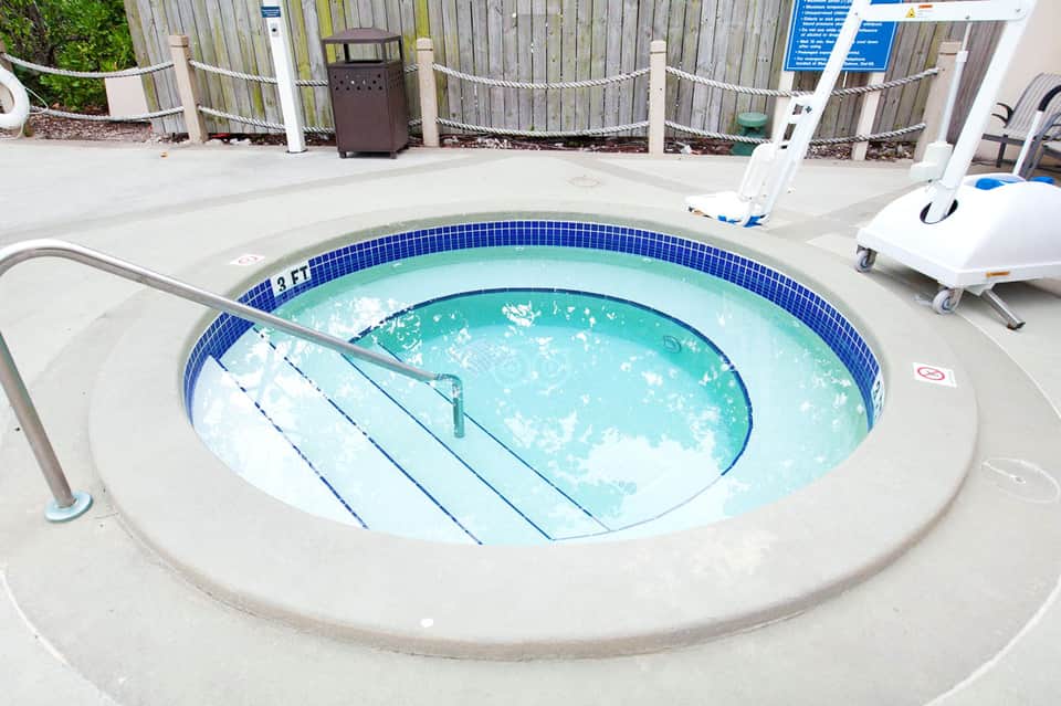 Circular hot tub with steps, surrounded by concrete deck and white loungers