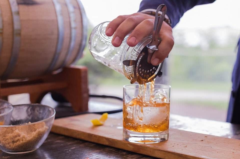 Person pouring whiskey from a glass decanter into a drink with ice
