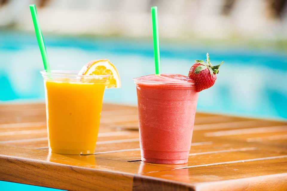 Two colorful tropical beverages with straws by poolside, orange juice and strawberry drink