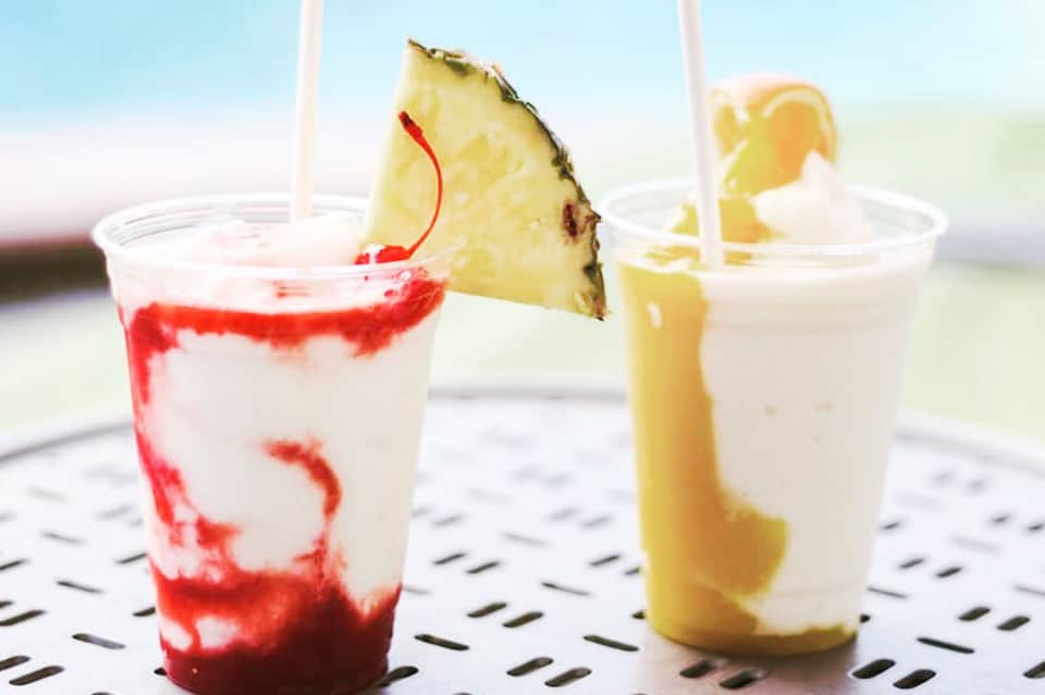 Three colorful tropical cocktails with pineapple and citrus garnishes on a perforated white surface