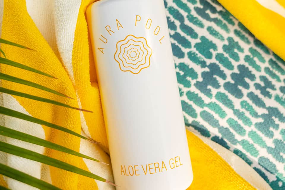 Aura Pool aloe vera gel product on colorful beach towels with palm leaves