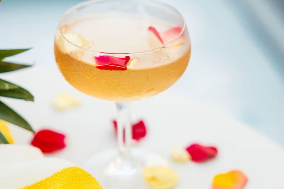 Golden cocktail with ice and flower petals in coupe glass with tropical garnish