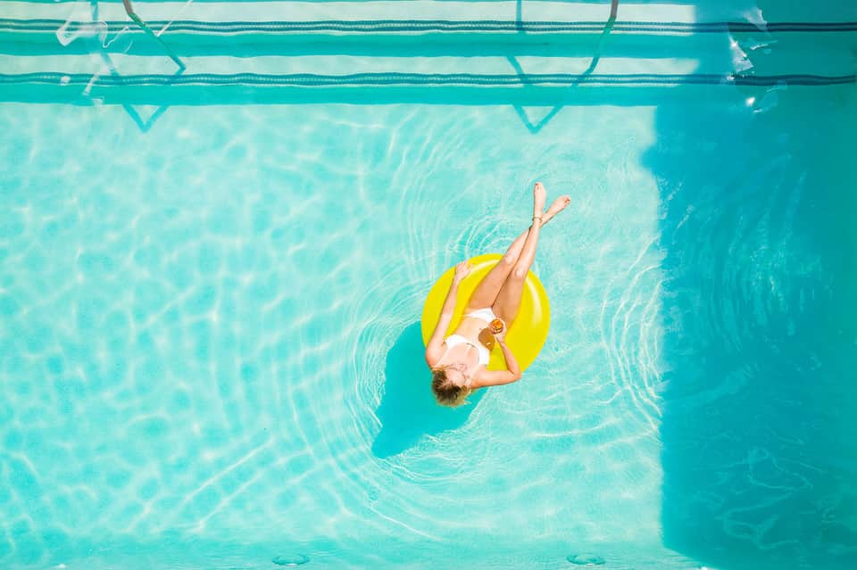 Aerial view of person floating on yellow ring in crystal-clear turquoise swimming pool