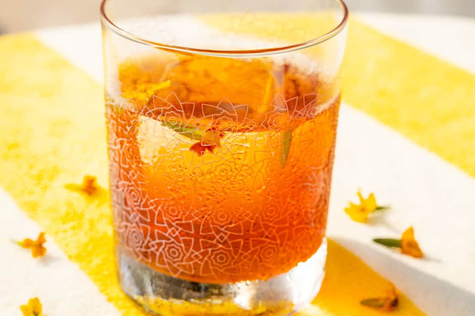 Glass of iced amber beverage on a yellow napkin with scattered yellow flower petals
