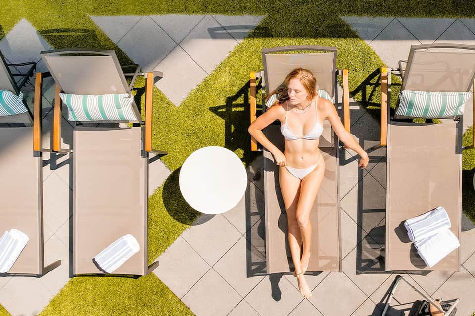 Aerial view of woman on sunbed in geometric poolside courtyard with green moss walls and umbrellas
