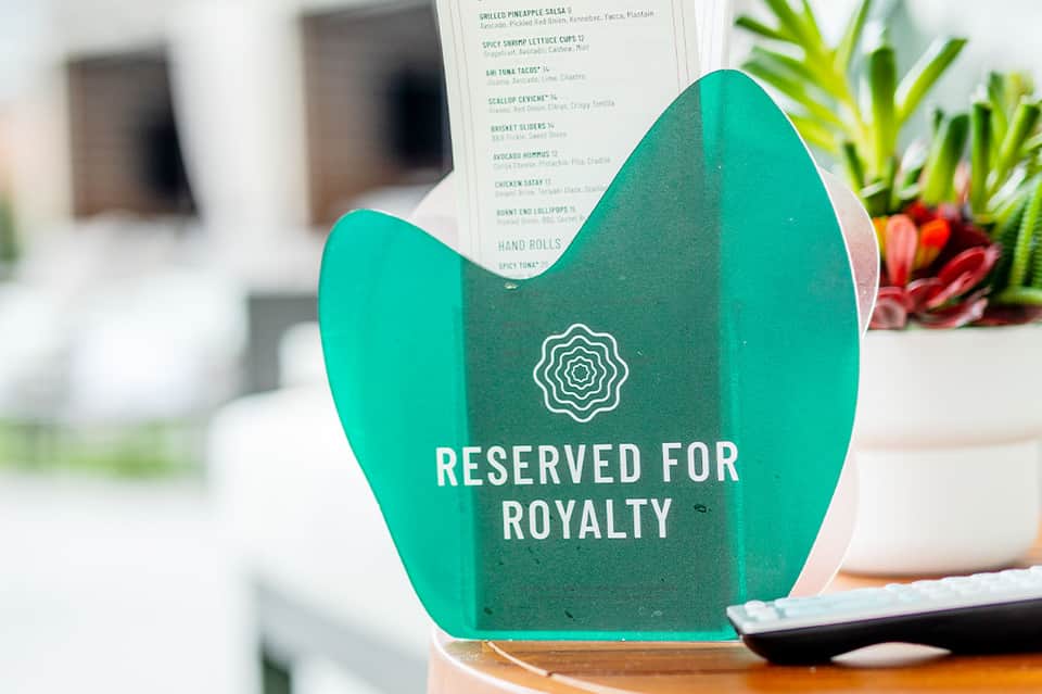 Green table tent sign reading 'Reserved for Royalty' on restaurant table with menu visible