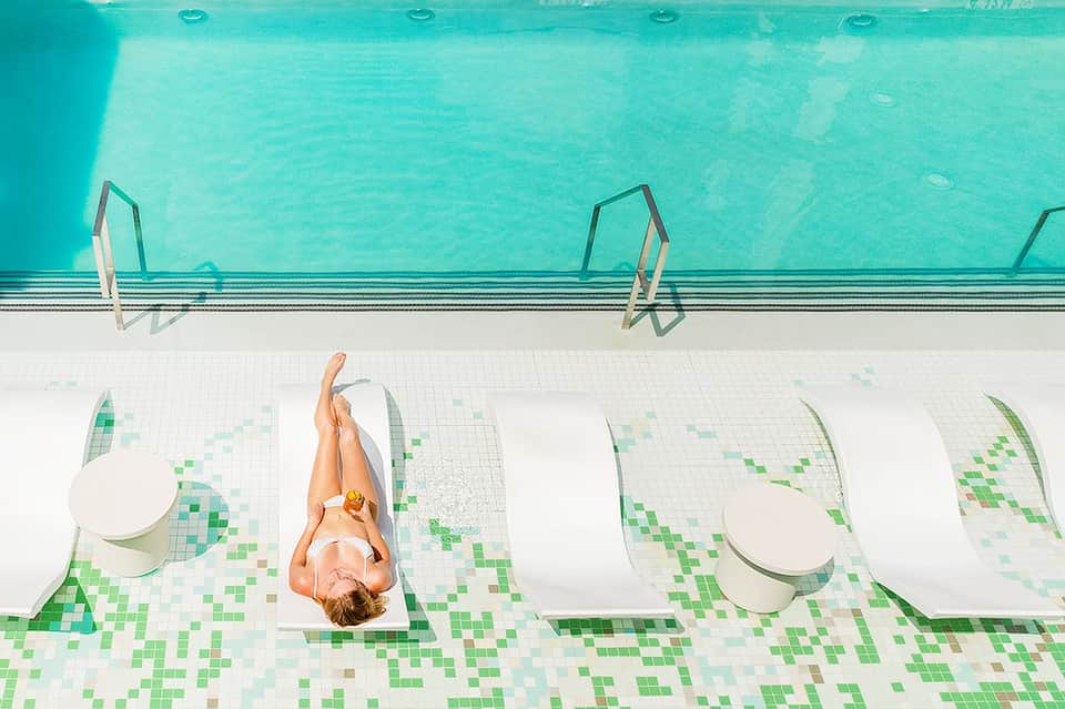 Overhead view of woman relaxing on white lounge chair beside turquoise swimming pool with metal railings