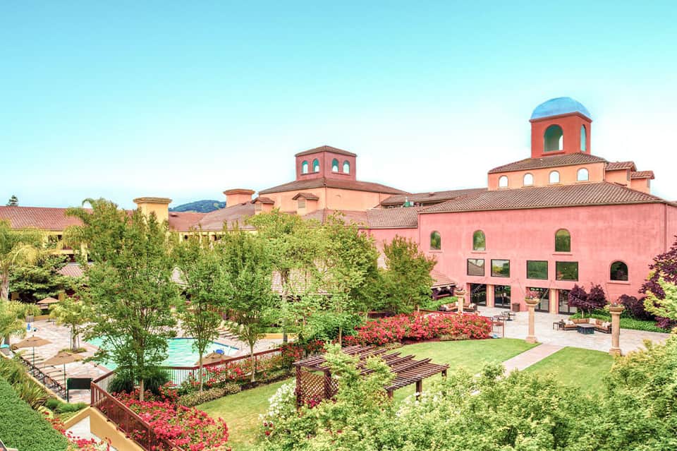 Pink Mediterranean-style resort building with manicured gardens, red flowers, and resort pool area