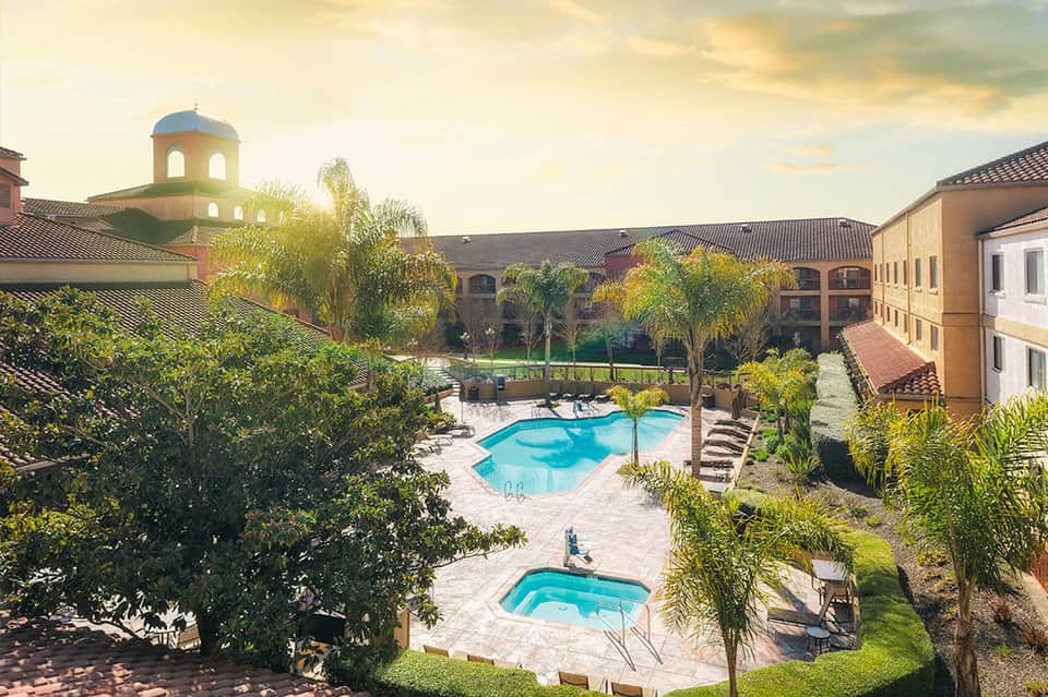Luxury resort courtyard with two pools, palm trees, Spanish architecture, and manicured grounds