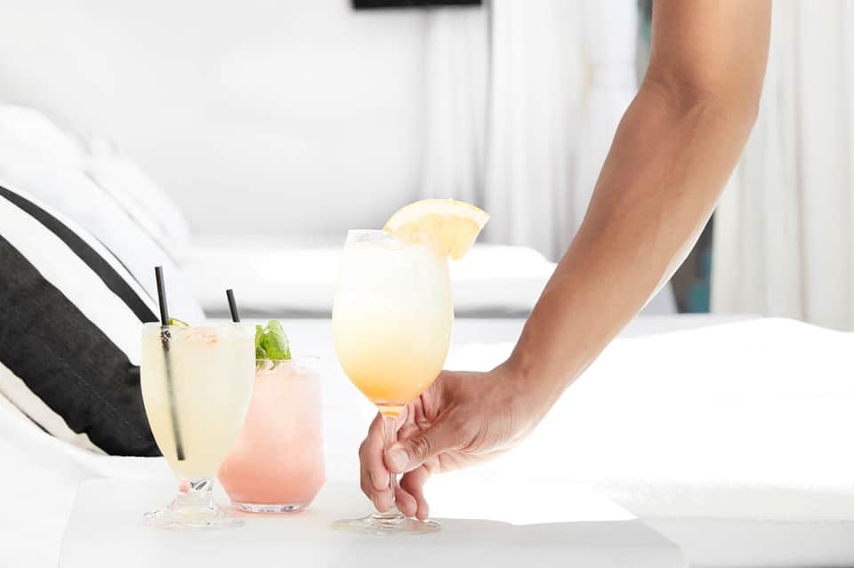 Server presenting three refreshing beverages - clear, pink, and yellow drinks with garnishes