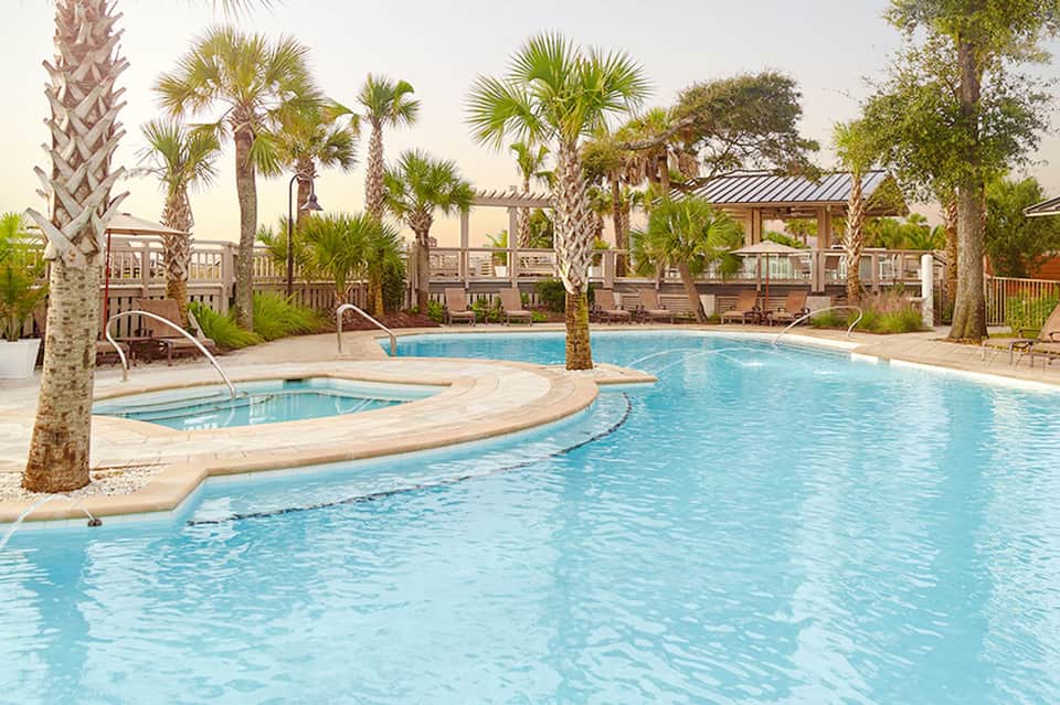 Resort pool with palm trees, spa tub, wooden pergola, and lounge seating areas