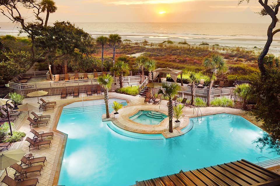 Aerial view of beachfront resort with multiple pools and palm trees at sunset