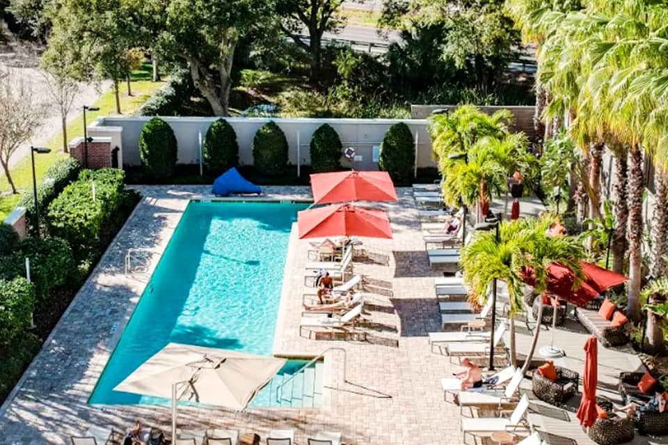 Aerial view of rectangular pool with red umbrellas, lounge chairs, and lush tropical landscaping