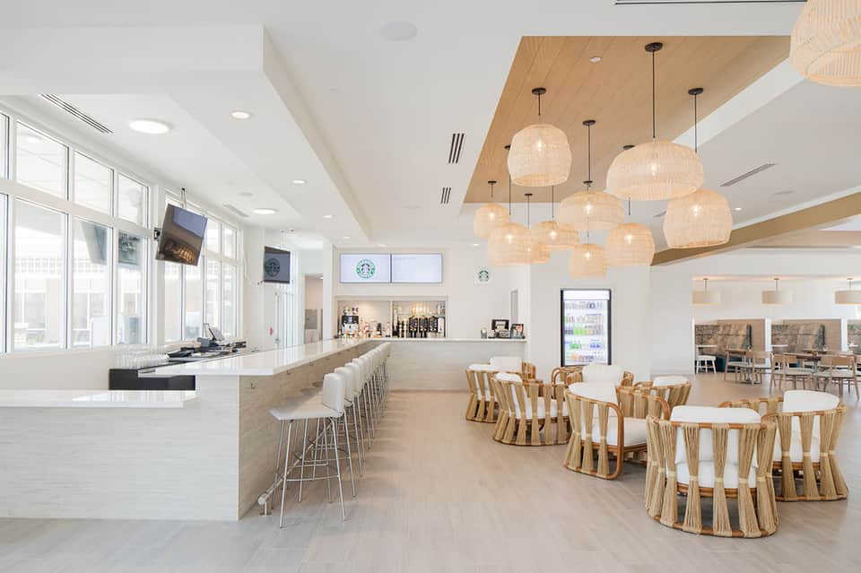 Modern hotel café interior with wooden ceiling, pendant lights, and woven chairs
