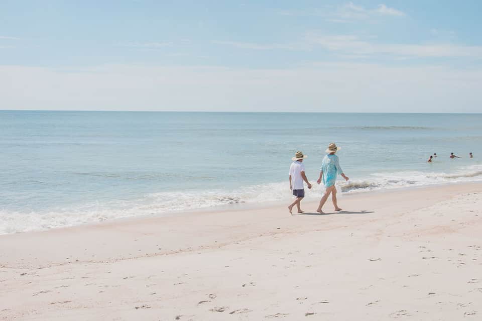 Two children walking along sandy beach toward clear turquoise ocean water on sunny day