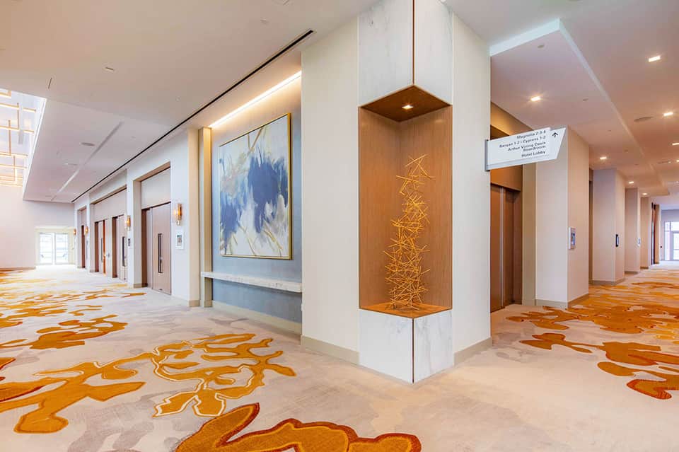 Modern hotel corridor with elegant flooring, wooden elevator doors, and contemporary wall art