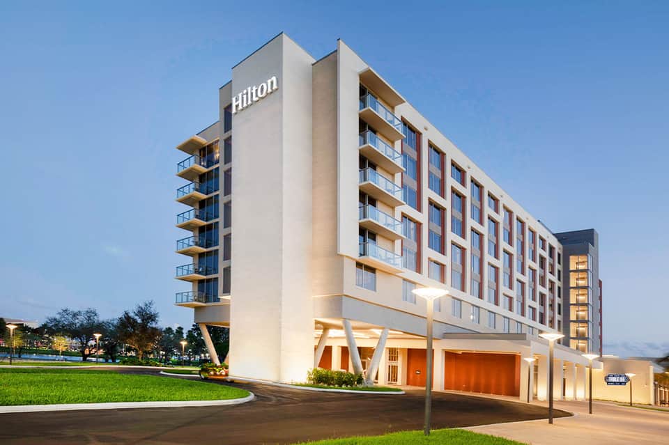 Modern Hilton hotel exterior at dusk with illuminated entrance, contemporary architecture, and green landscaping