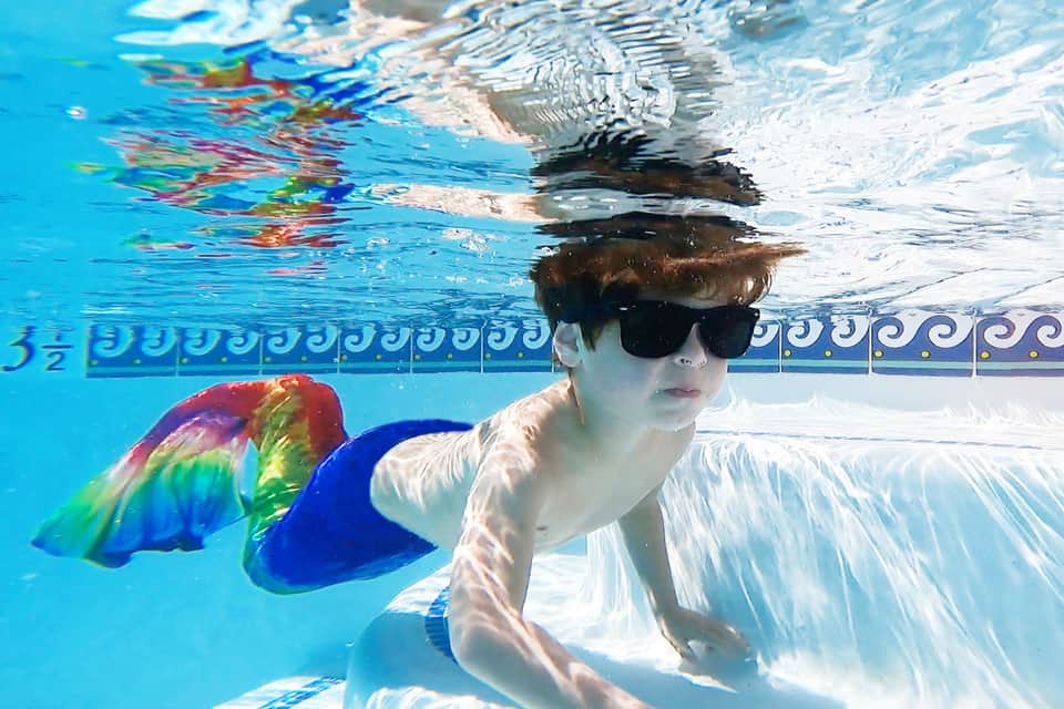 Child swimming underwater wearing goggles and colorful fins in a bright blue pool
