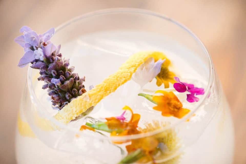 Elegant cocktail garnished with lavender sprig and colorful edible flowers in a clear glass