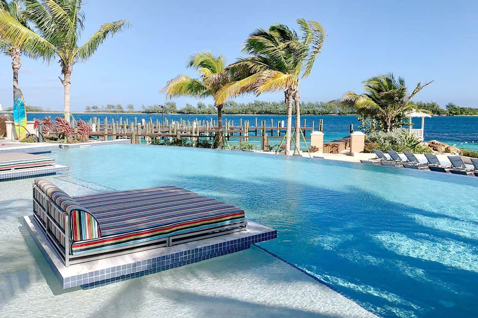 Lagoon-style pool with striped lounger, palm trees, and wooden dock overlooking turquoise ocean water