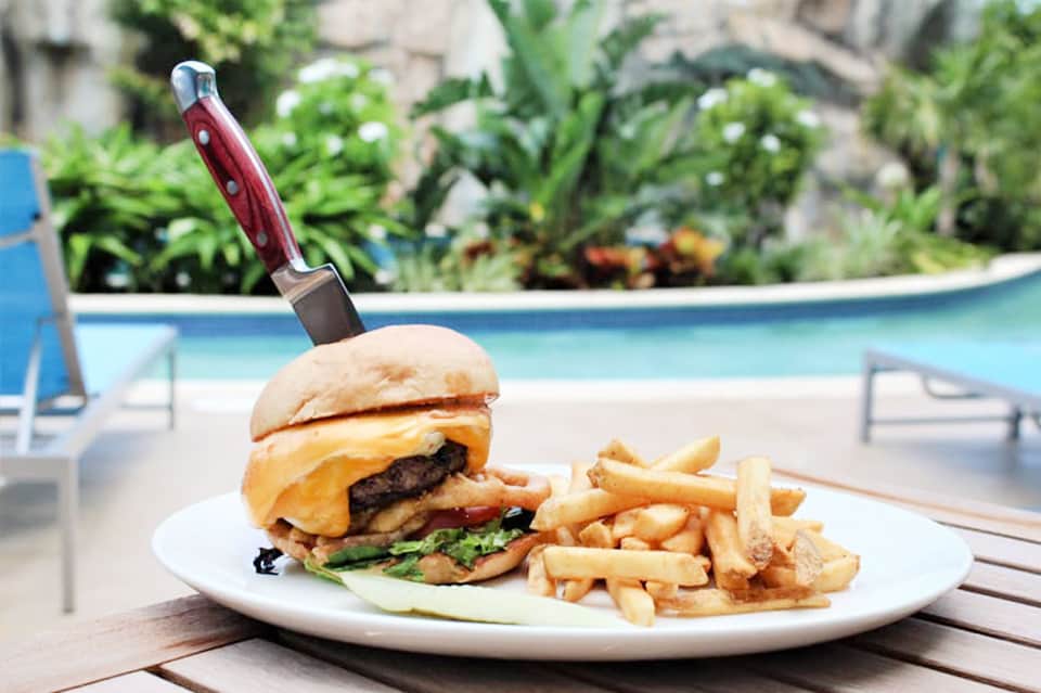 Gourmet burger and fries plated poolside with knife garnish