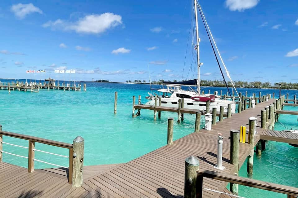 Sailboat docked at a wooden pier with turquoise water and tropical islands in the background