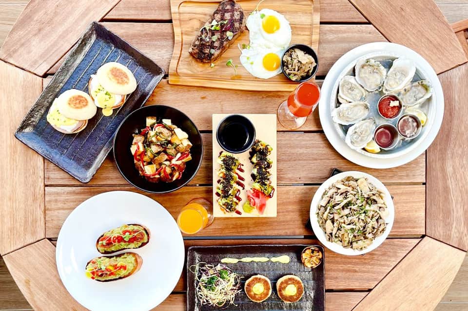 Overhead view of brunch spread with oysters, eggs, avocado toast, and seafood on wooden table