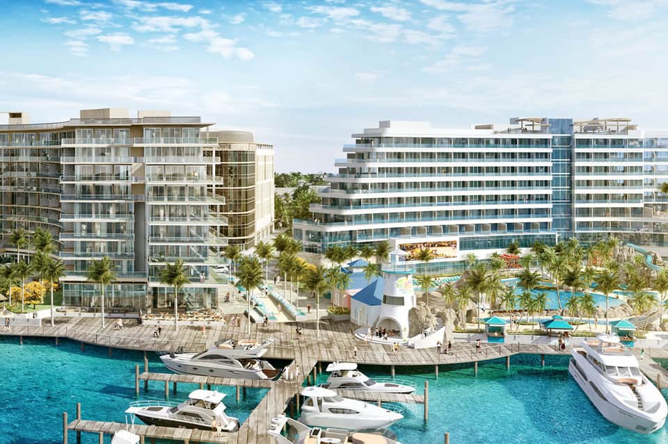 Waterfront resort development with modern buildings, marina, boats, and turquoise water