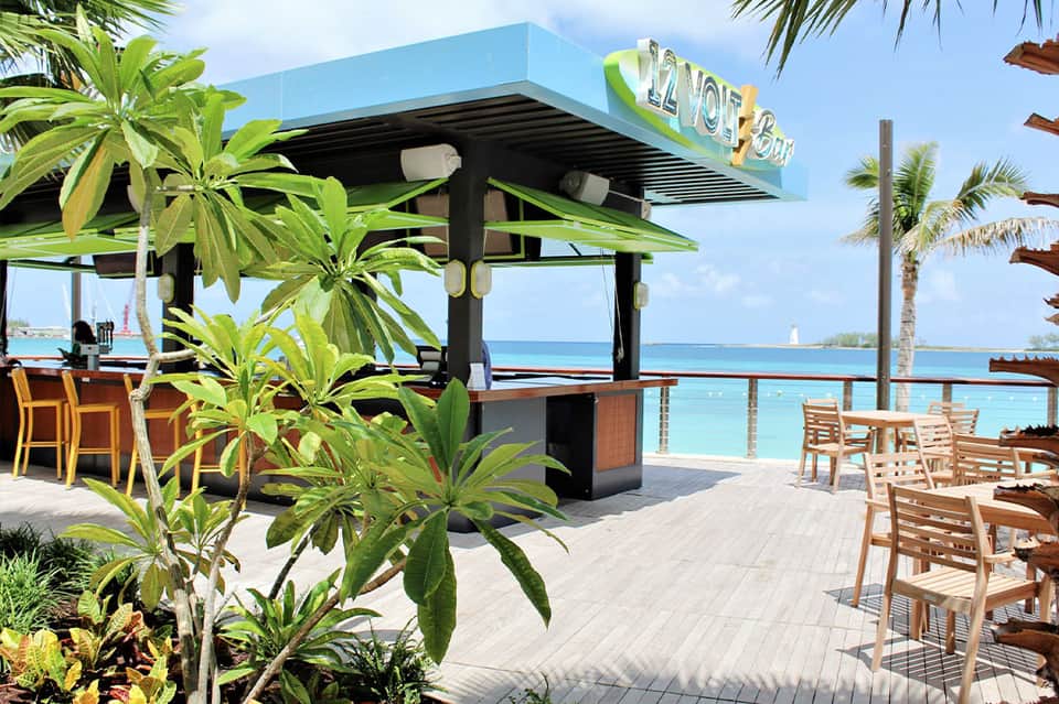 Beachfront bar with blue signage, palm trees, ocean views, and wooden seating area